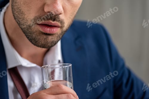 Preview: cropped view of bearded man holding glass of water while suffering from heat on grey