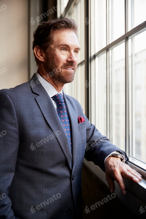 Preview: Senior white businessman looking out of window, vertical