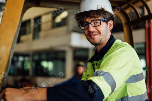 Preview: Male industrial engineer in white hard hat driving forklift at manufacturing