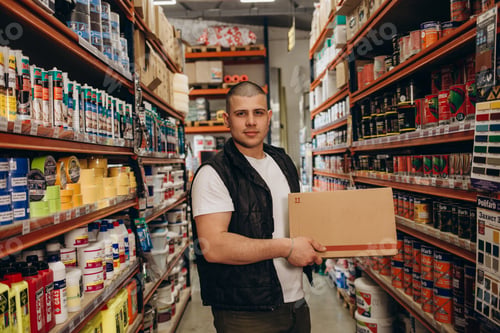 Preview: Caucasian consultant in uniform at hardware store. Male standing next to shelves with tools at store