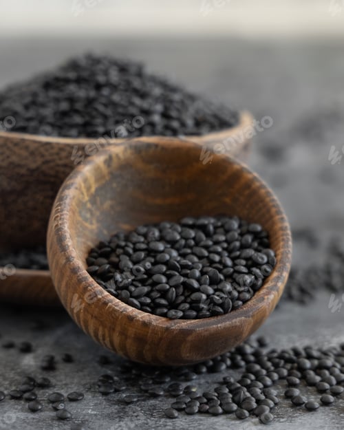 Preview: Wooden bowls of dry black lentils beans on grey table close up, protein source for vegetarian diet