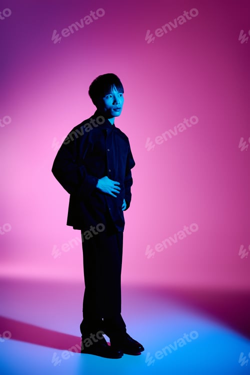 Preview: Stylish young asian man poses confidently against vibrant colored background at twilight