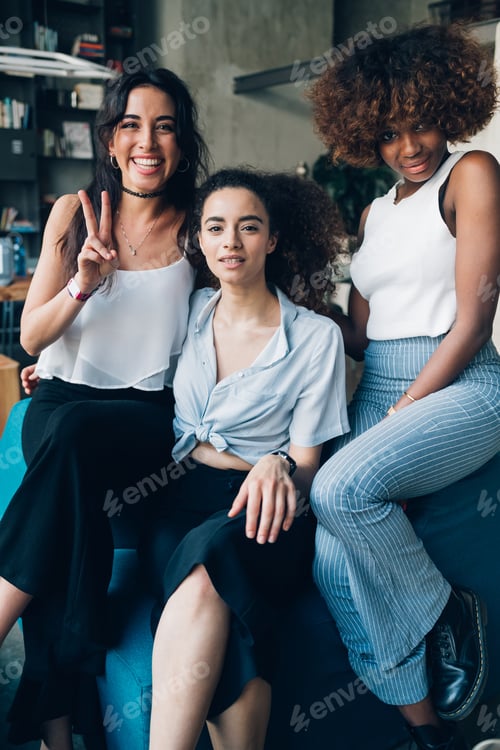 Preview: three young multiracial women sitting together in modern loft and looking camera