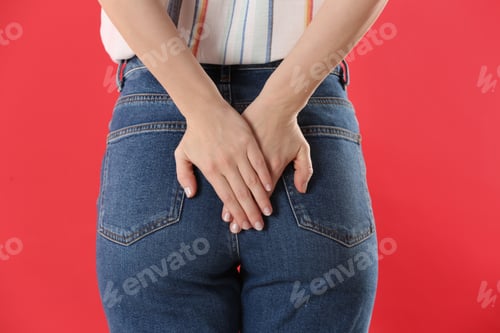 Preview: Woman suffering from hemorrhoid on red background, closeup