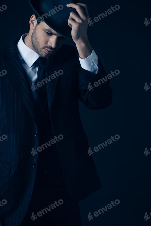 Preview: Thoughtful mafioso holding felt hat on dark blue