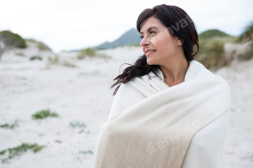 Preview: Thoughtful woman wrapped in shawl on beach