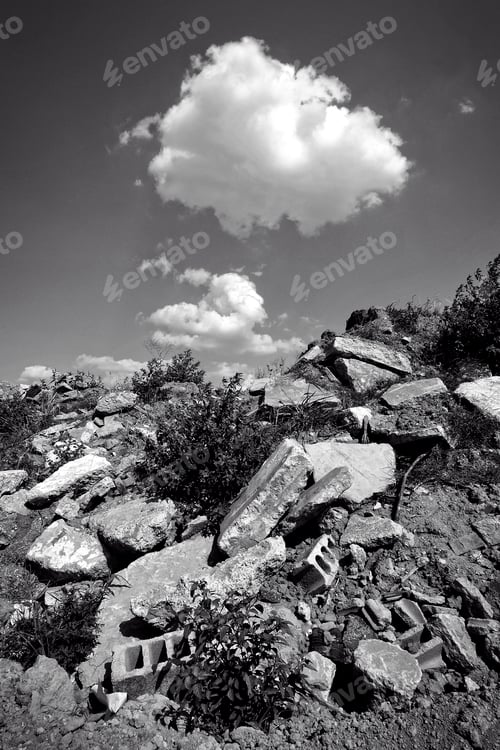 Preview: Black and white shot of a pile of rubble under a cloud in the sky.