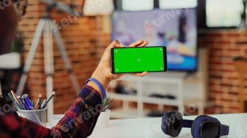 Preview: Female freelancer holding smartphone with horizontal greenscreen