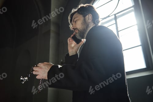 Preview: Middle Aged Caucasian Man Praying with Rosary While Talking on Smartphone