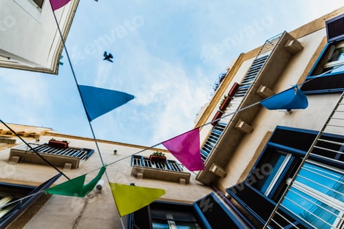 Preview: Colorful pennants seen from below crossing a street with old buildings.