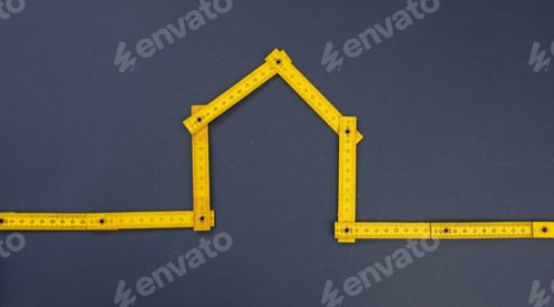 Preview: Home shape yellow wooden measure on blue background. Close up view.