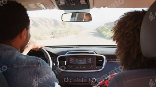 Preview: Rear View Of Young Couple On Road Trip Driving Rental Car Along Country Road