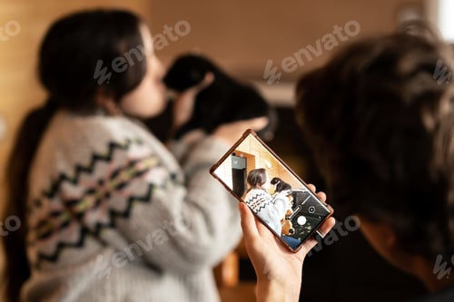 Preview: A guy take a photo on a phone camera as a girl kisses a small black puppy