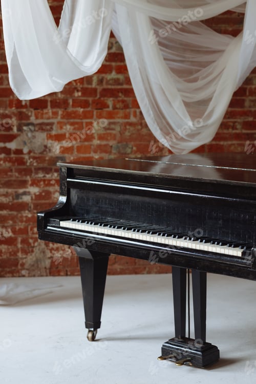 Preview: Old black grand piano in loft room with red brick wall and white fabric drapes