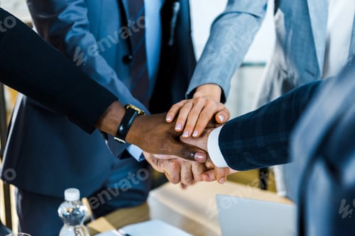 Preview: cropped view of multicultural men and businesswomen putting hands together