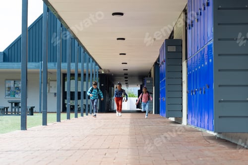 Preview: Three students walk through a school corridor lined with blue lockers with copy space