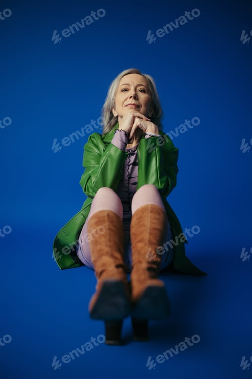 Preview: full length of trendy senior woman in green leather jacket and brown suede boots looking at camera