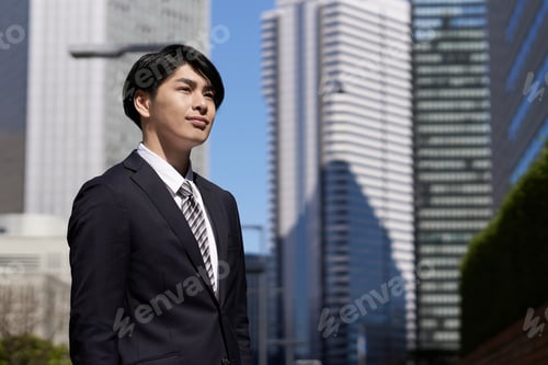 Preview: A smiling Japanese male businessman stands in an office district.