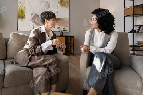 Preview: Two businesswomen discussing sitting on armchairs in modern office