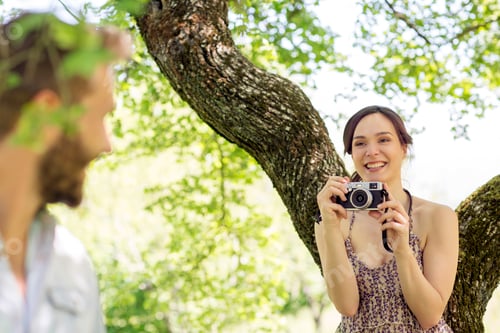 Preview: Young woman underneath tree taking photograph of young man