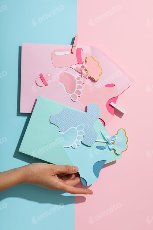 Preview: Envelopes with paper baby things and hand on blue and pink background, top view
