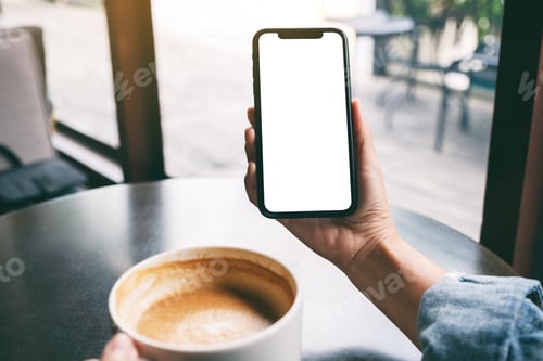 Preview: a woman holding black mobile phone with blank screen while drinking coffee on the table