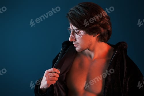 Preview: Beautiful long haired hot man in glasses is in the studio with blue neon lighting