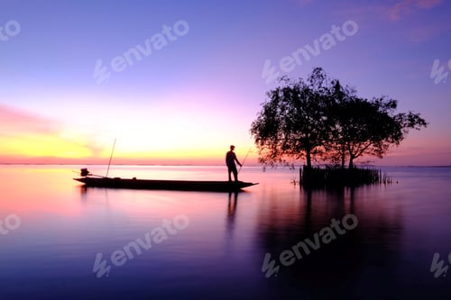 Preview: Silhouette image of a fisherman standing in his boat in the sea at dawn