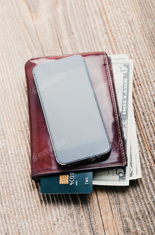 Preview: Smartphone with blank screen, wallet, dollar banknotes, debit credit cards and notebook on table