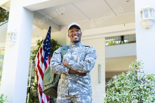 Preview: Happy african american male soldier with arms crossed in cap outside home with usa flag, copy space