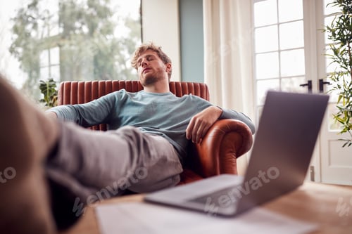 Preview: Tired Man Sleeping In Armchair With Feet Up At Home With Laptop In Foreground