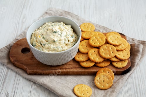 Vista previa: Dip casero de cebolla caramelizada y espinacas con galletas redondas saladas, vista lateral.