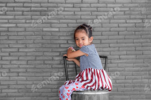 Preview: portrait of a little child girl stands smiling looking into the camera's on gray brick wall