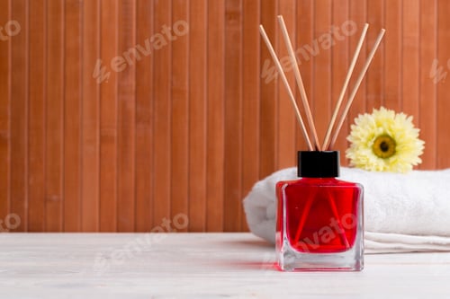 Preview: Red scented diffuser with wooden sticks and a flower on a white towel, creating a calm atmosphere