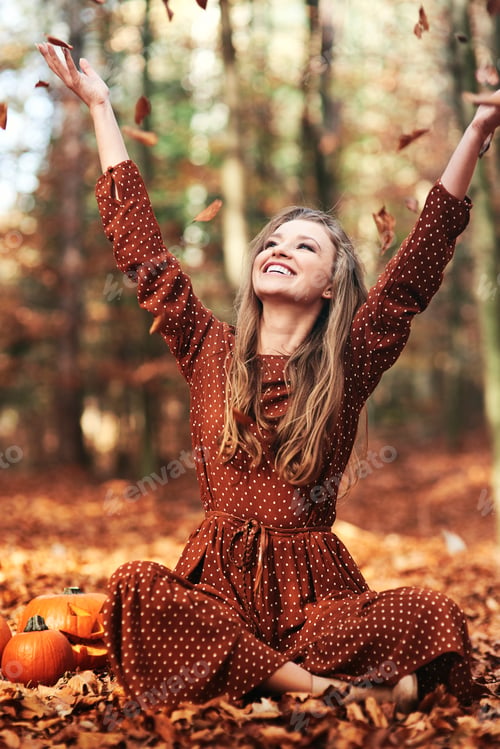 Preview: Happy woman sitting and throwing autumn leaves in the forest