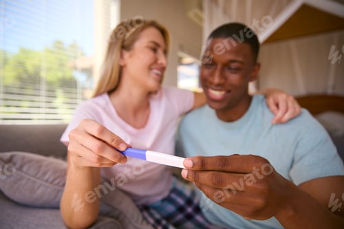 Preview: Excited Multi-Racial Couple In Bedroom At Home Celebrating Positive Pregnancy Test Result