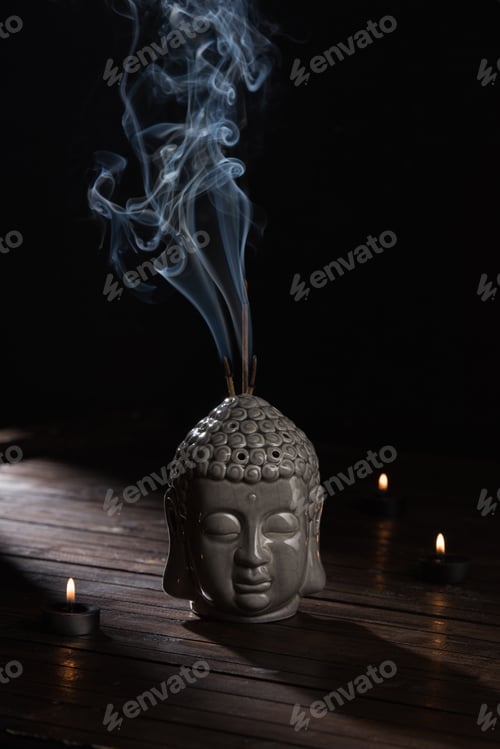 Preview: sculpture of buddha head with burning incense sticks and candles on table