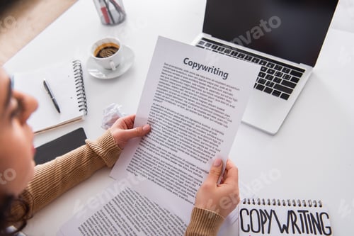 Preview: Blurred copywriter holding paper near laptop and coffee at home