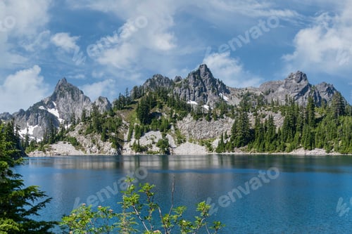 Preview: Jagged mountain peaks over pristine blue alpine lake in pine forest.