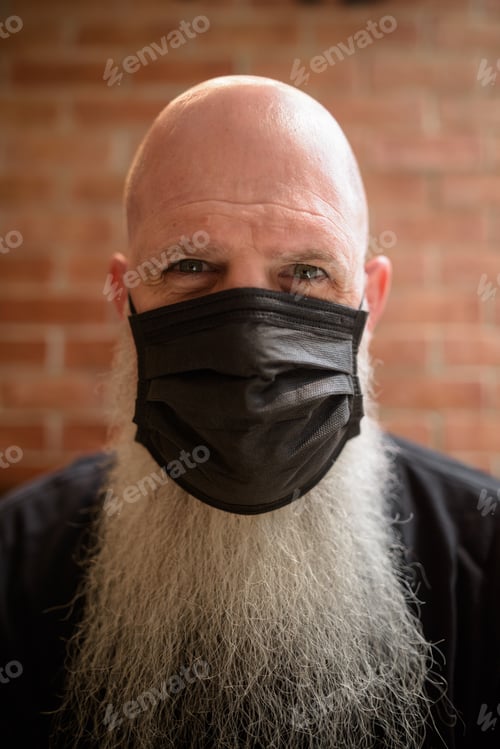 Preview: Mature man with long gray beard wearing face mask to protect from corona virus Covid 19