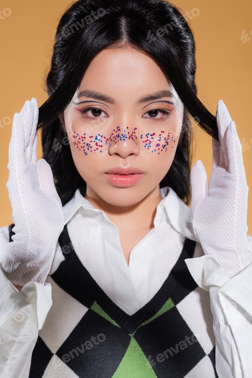 Preview: Portrait of asian model with makeup posing and looking at camera isolated on orange