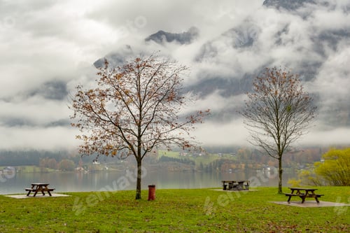 Preview: Moody autumn landscape with bare trees and benches on mountain lake shore.