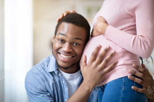 Preview: Handsome black man listening his wife's pregnant belly at home