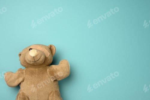 Preview: Old teddy bear with a band-aid on the eye lies on a blue background