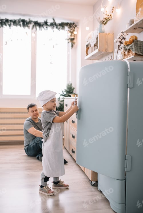 Preview: Young man and his son with oven sheet in kitchen. Father with little son on the kitchen.