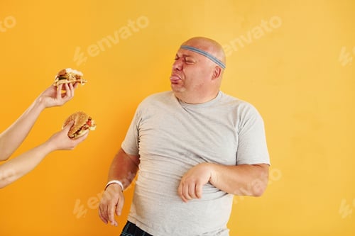 Preview: Funny overweight man in sportive head tie is against yellow background