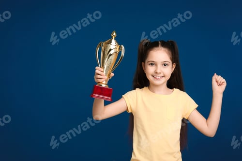 Preview: Happy girl with golden winning cup on dark blue background. Space for text