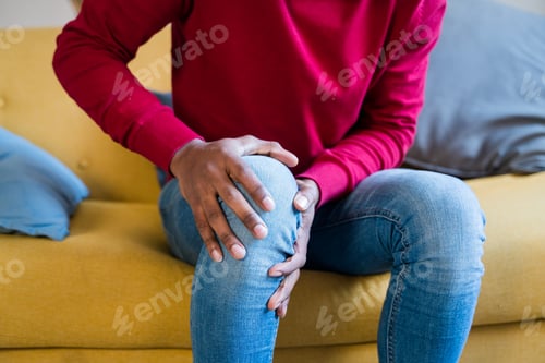 Preview: Cheerful black man sitting on sofa with knee pain