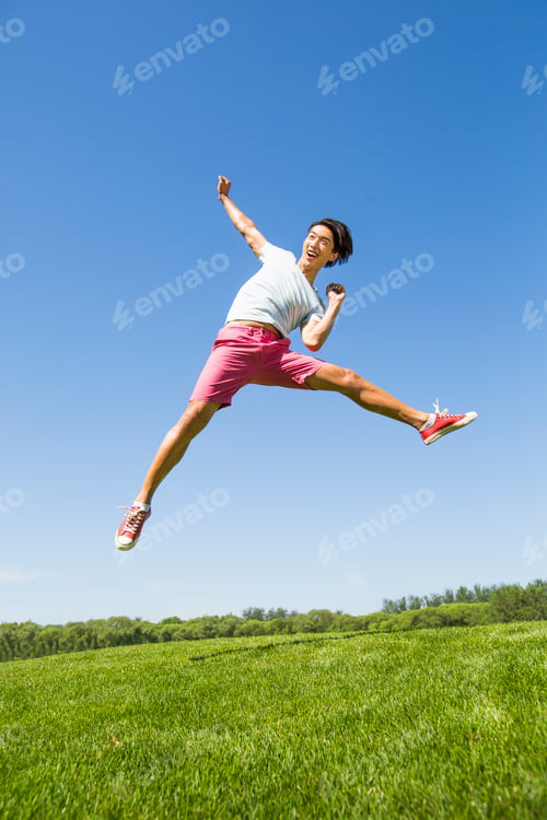Preview: Cheerful young Chinese man jumping on grass