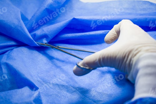 Preview: Closeup of a surgeon wearing a latex glove and holding forceps against a blue background